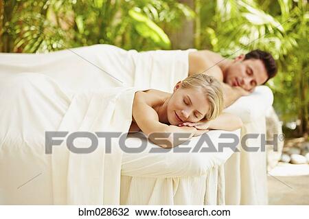 Stock Image - Couple laying on massage tables outdoors. Fotosearch