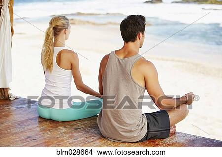 Picture - Couple meditating together on patio overlooking ocean. Fotosearch