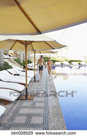 Stock Photo - Couple walking by swimming pool. Fotosearch