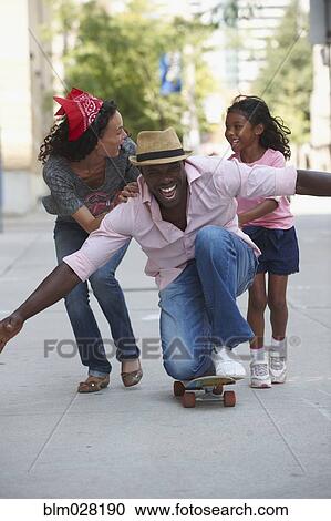 Stock Image - Family playing on skateboard on urban sidewalk. Fotosearch