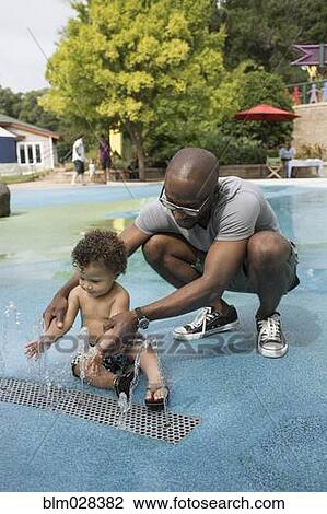 Stock Image - Father and toddler son playing in fountain. Fotosearch