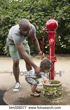 Stock Photo - Father and toddler son using water fountain in park. Fotosearch