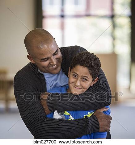 Stock Image - Father hugging son indoors. Fotosearch