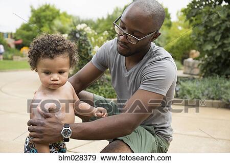 Father putting sunscreen on toddler son in park View Large Photo Image Stock Photo - Father putting sunscreen on toddler son in park. Fotosearch