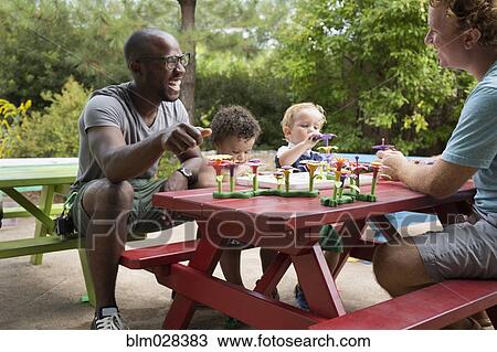 Stock Image - Fathers and toddler sons playing at picnic table. Fotosearch