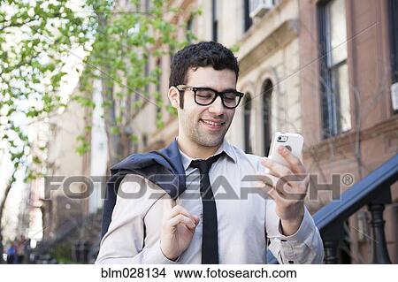 Picture - Hispanic businessman using cell phone outside. Fotosearch