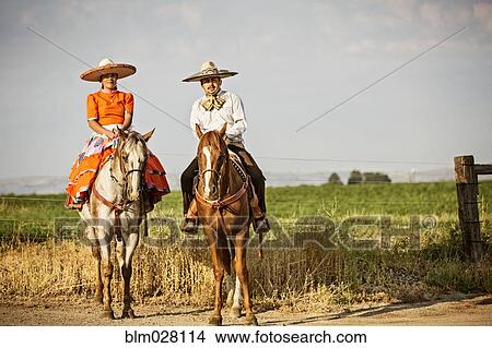 Picture - Hispanic couple in traditional clothing on horseback. Fotosearch
