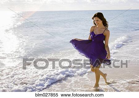 Stock Photography - Hispanic woman walking in surf on beach. Fotosearch