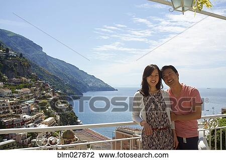 Stock Image - Korean couple overlooking hillside city, Positano, Campania, Italy. Fotosearch
