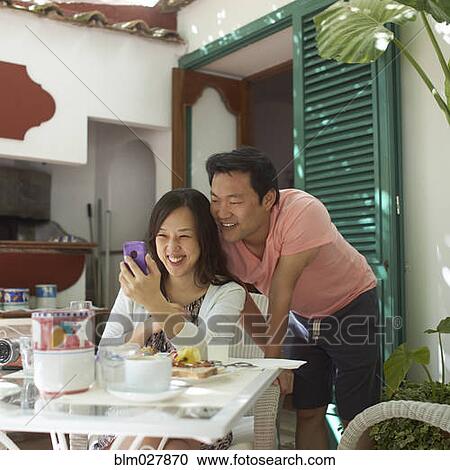 Stock Image - Korean couple using cell phone at breakfast. Fotosearch