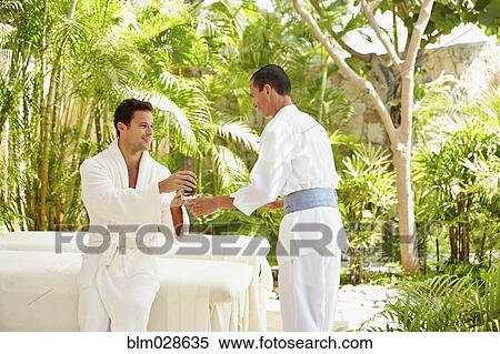 Stock Photography - Man being served drink at massage table outdoors. Fotosearch