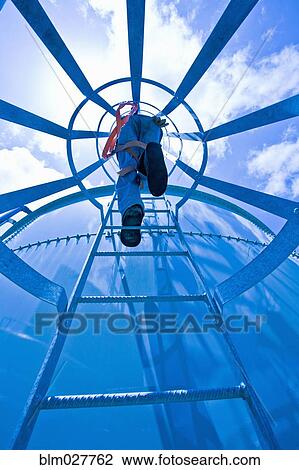Stock Image - Man climbing water tower ladder. Fotosearch