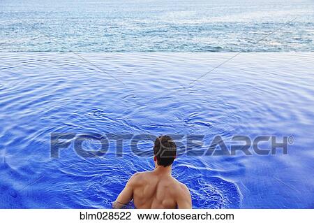 Stock Image - Man relaxing in infinity pool. Fotosearch
