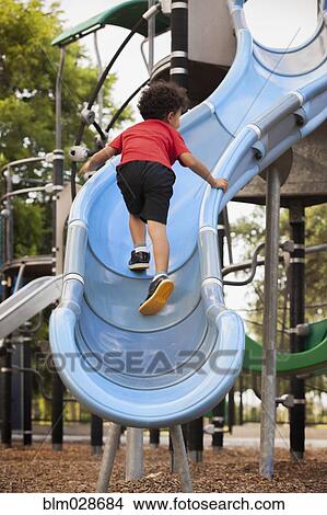 Picture - Mixed race boy climbing slide at playground. Fotosearch