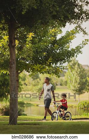 Mixed race father and son with bicycle in park View Large Photo Image Stock Photograph - Mixed race father and son with bicycle in park. Fotosearch