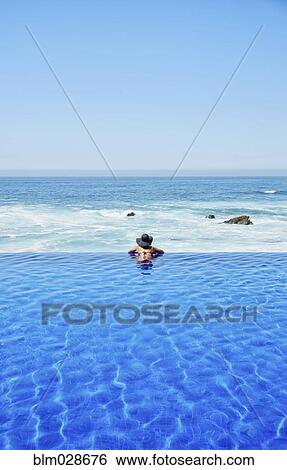 Stock Photograph - Mixed race woman relaxing in infinity pool. Fotosearch