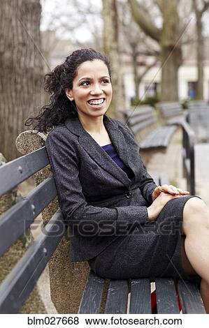 Stock Photo - Mixed race woman sitting on park bench. Fotosearch
