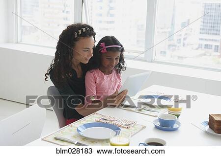 Mother and daughter using digital tablet at table View Large Photo Image Stock Image - Mother and daughter using digital tablet at table. Fotosearch