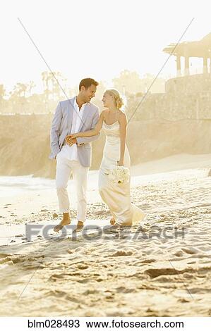 Stock Image - Newlywed couple holding hands on beach. Fotosearch