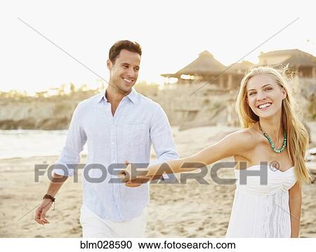 Stock Image - Newlywed couple holding hands on beach. Fotosearch