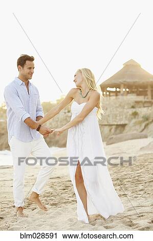 Stock Image - Newlywed couple holding hands on beach. Fotosearch