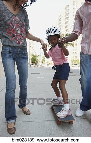 Parents helping daughter ride skateboard on urban sidewalk View Large Photo Image Stock Photo - Parents helping daughter ride skateboard on urban sidewalk. Fotosearch