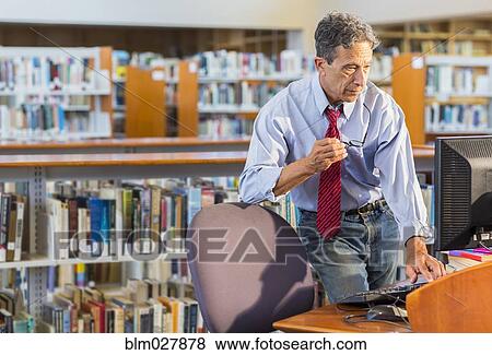 Stock Photo - Senior man working at computer in library. Fotosearch