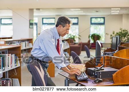 Stock Photo - Senior man working on computer in library. Fotosearch
