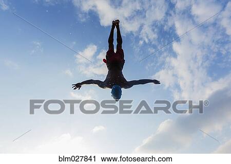 Stock Image - Silhouette of man diving against blue sky. Fotosearch
