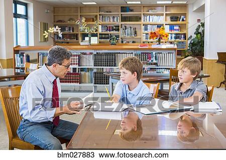 Stock Image - Teacher and students working in library. Fotosearch