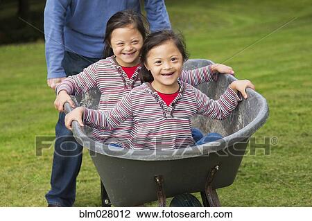 Stock Image - Twins with Down's Syndrome smiling in wheelbarrow. Fotosearch