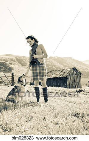 Stock Image - Woman petting dog in rural landscape. Fotosearch