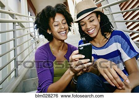 Stock Photograph - Women using cell phone together on steps. Fotosearch