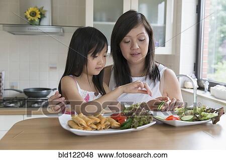 Asian mother and daughter eating in kitchen View Large Photo Image Stock Photo - Asian mother and daughter eating in kitchen. Fotosearch