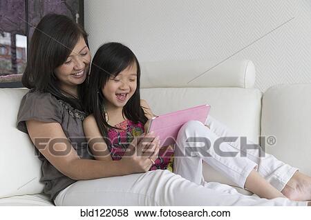 Stock Photo - Asian mother and daughter using digital tablet on sofa. Fotosearch