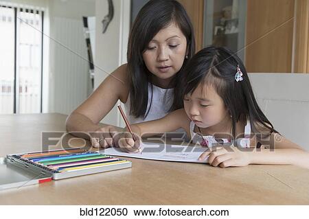 Stock Image - Asian mother watching daughter coloring. Fotosearch