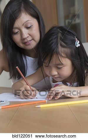 Stock Image - Asian mother watching daughter coloring. Fotosearch