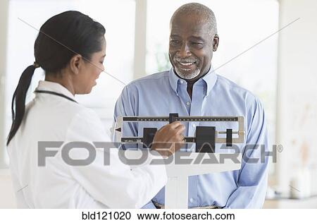 Stock Image - Black doctor weighing patient. Fotosearch