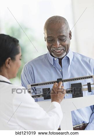Stock Photo - Black doctor weighing patient. Fotosearch