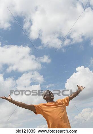 Stock Image - Black man with arms outstretched outdoors. Fotosearch
