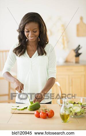 Stock Photography - Black woman chopping vegetables in kitchen. Fotosearch