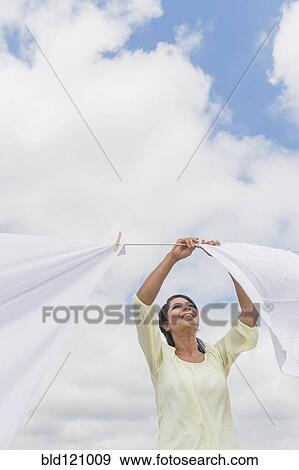 Stock Photo - Black woman hanging sheets from clothesline. Fotosearch
