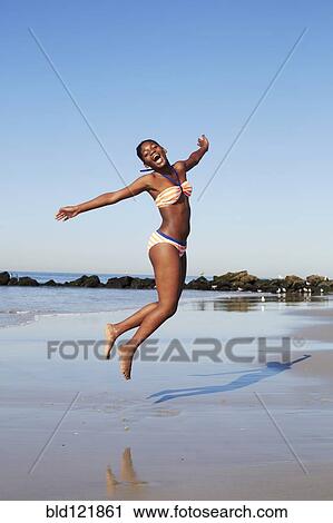 Stock Image - Black woman jumping for joy on beach. Fotosearch