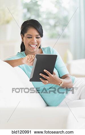 Stock Image - Black woman using digital tablet on sofa. Fotosearch