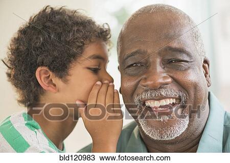 Stock Image - Boy whispering in grandfather's ear. Fotosearch