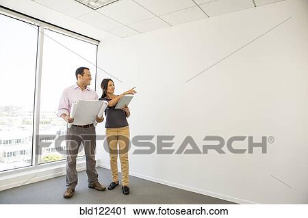 Stock Image - Business people examining blueprints in office. Fotosearch