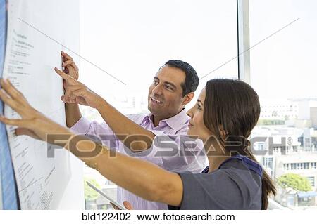 Stock Image - Business people examining blueprints in office. Fotosearch