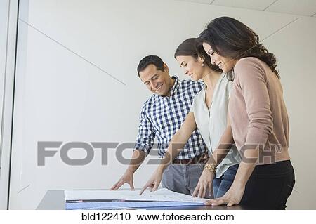 Stock Image - Business people examining blueprints in office. Fotosearch