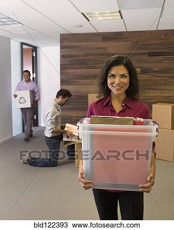 Stock Image - Businesswoman carrying boxes in office. Fotosearch