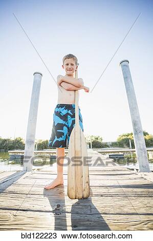 Stock Image - Caucasian boy holding paddle on dock. Fotosearch